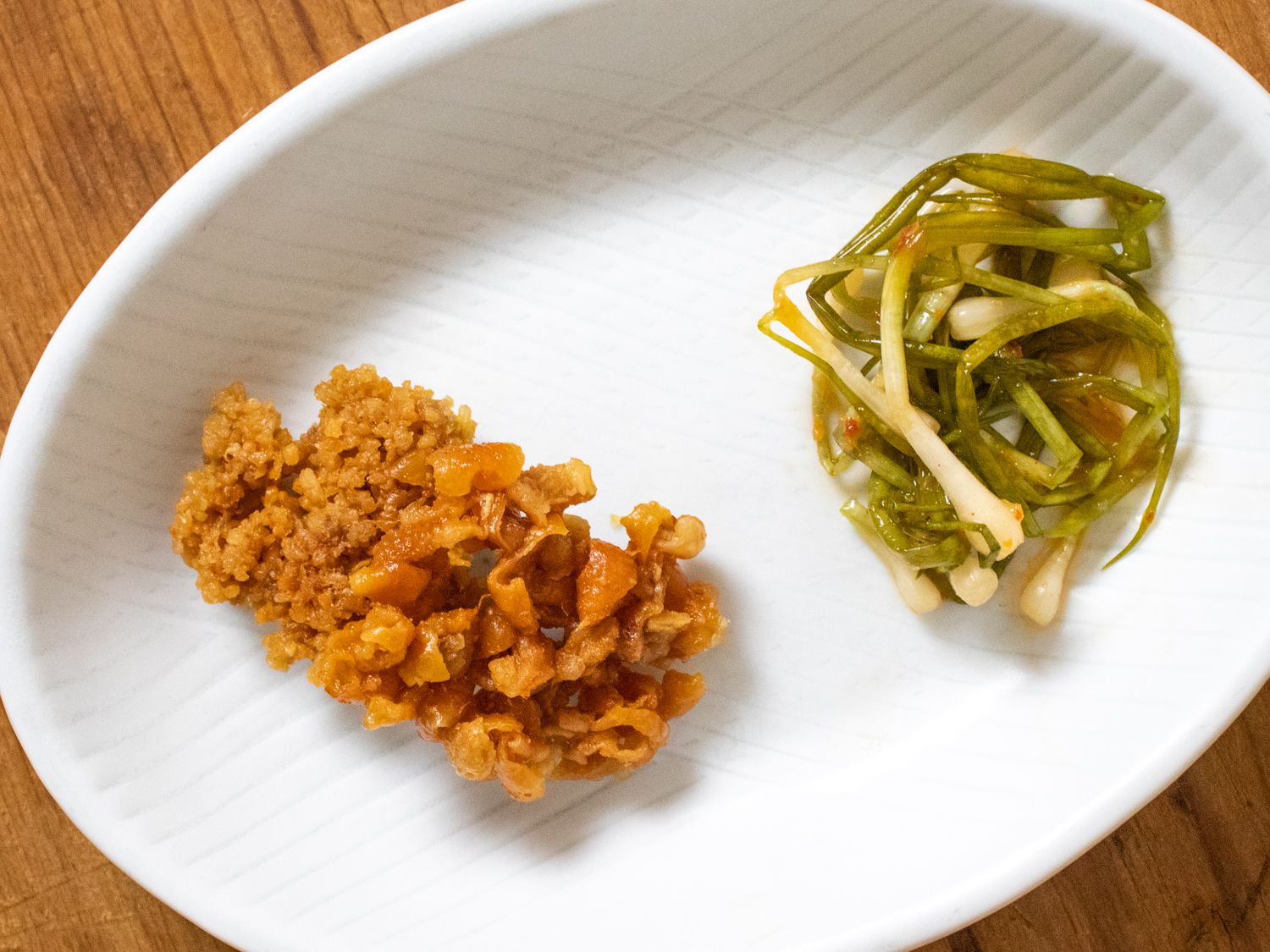 Little chicken skin chips on a plate with a pile of naga negi kimchi
