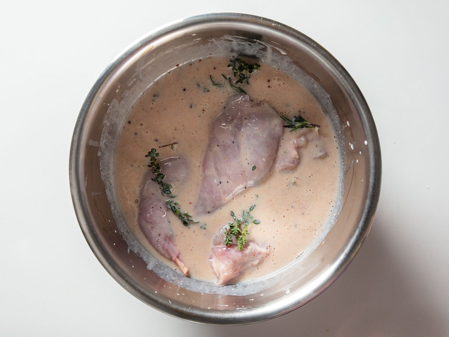 Rabbit pieces submerged in a bowl of buttermilk brine