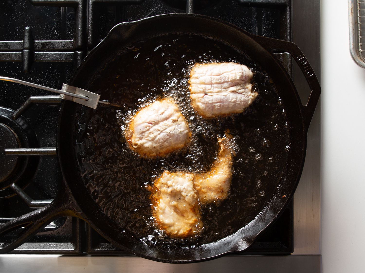 Overhead photo of second batch of brined and dredged chicken being fried in a cast iron skillet