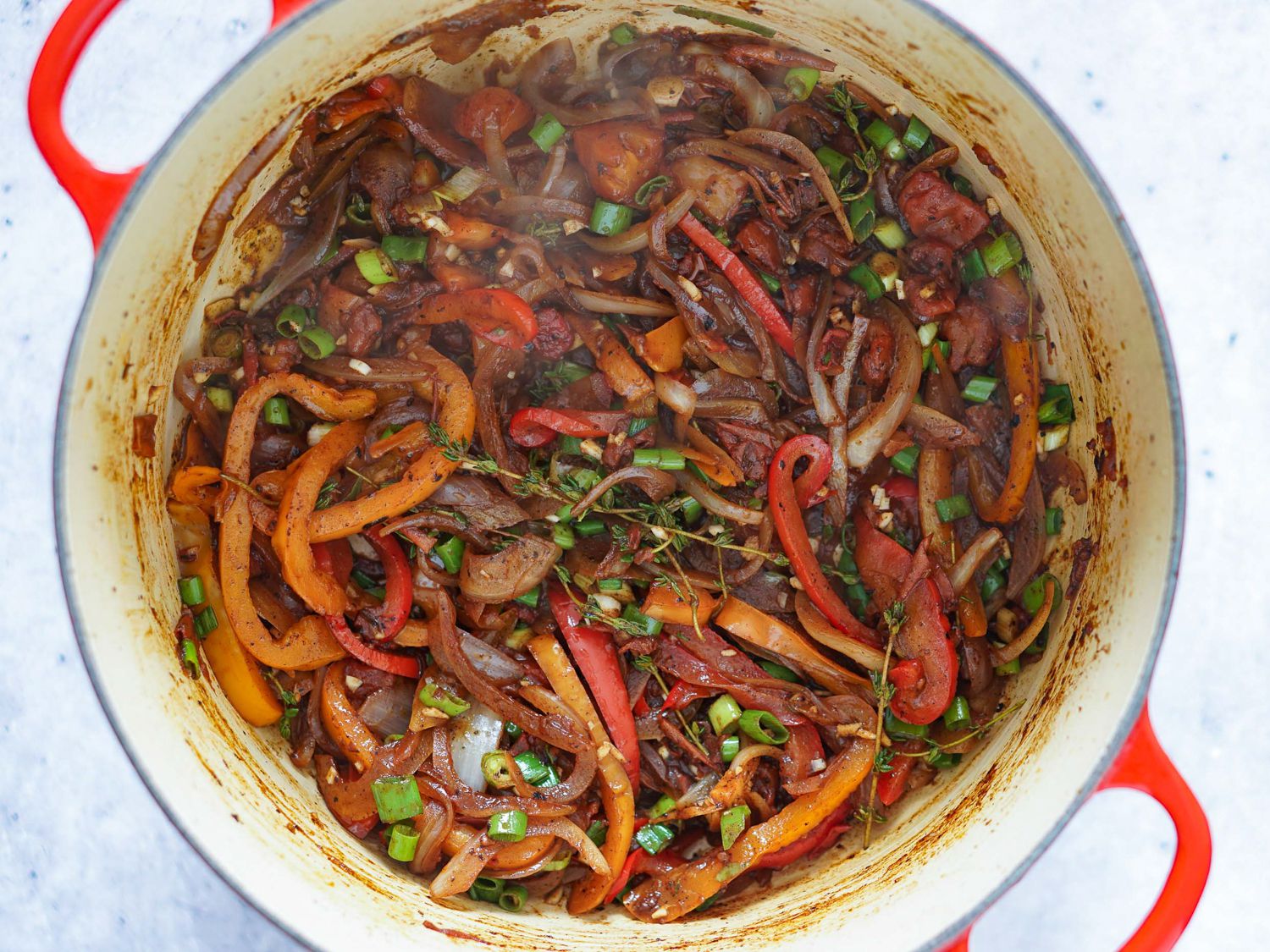 Peppers, onions, scallions, garlic, and thyme being sautéd in a Dutch oven