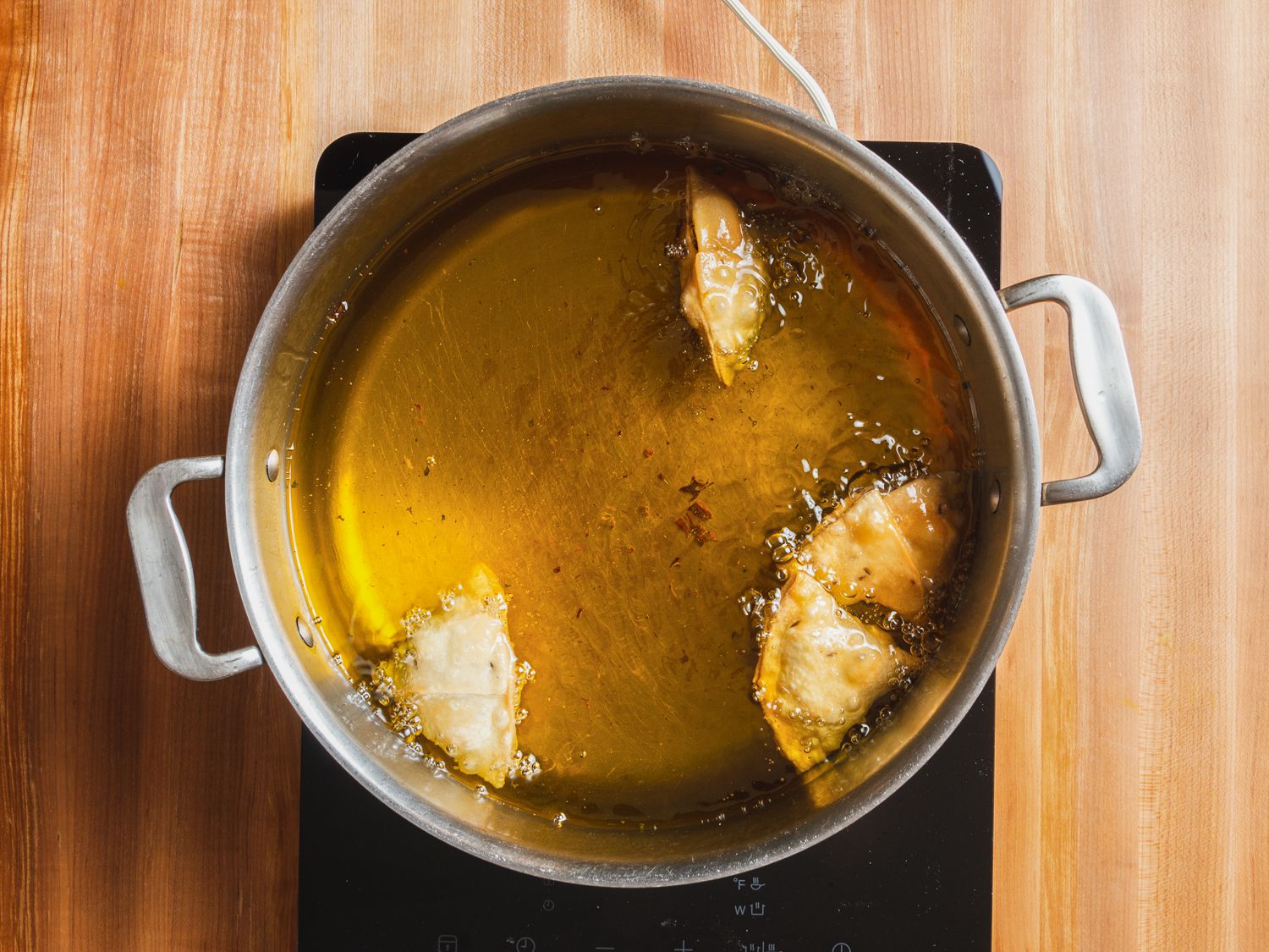 Kheema samosas viewed from overhead, frying in a pot of oil