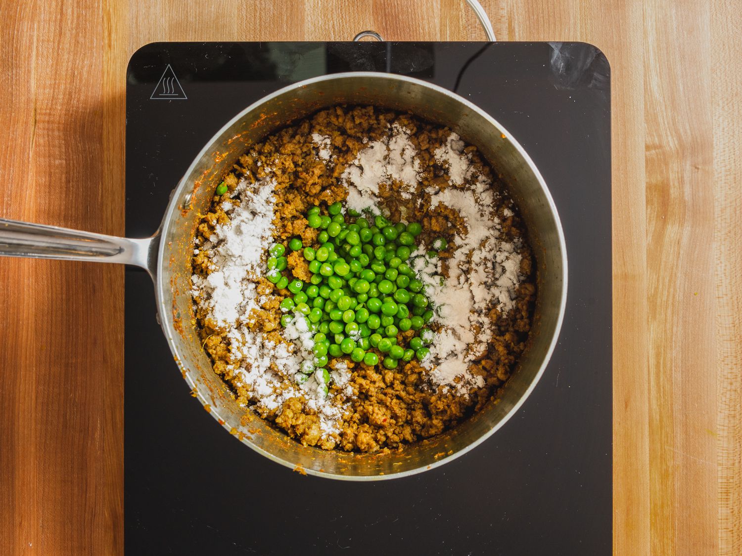 Overhead photo of peas and flour added on top of lamb kheema mixture in a saucepan