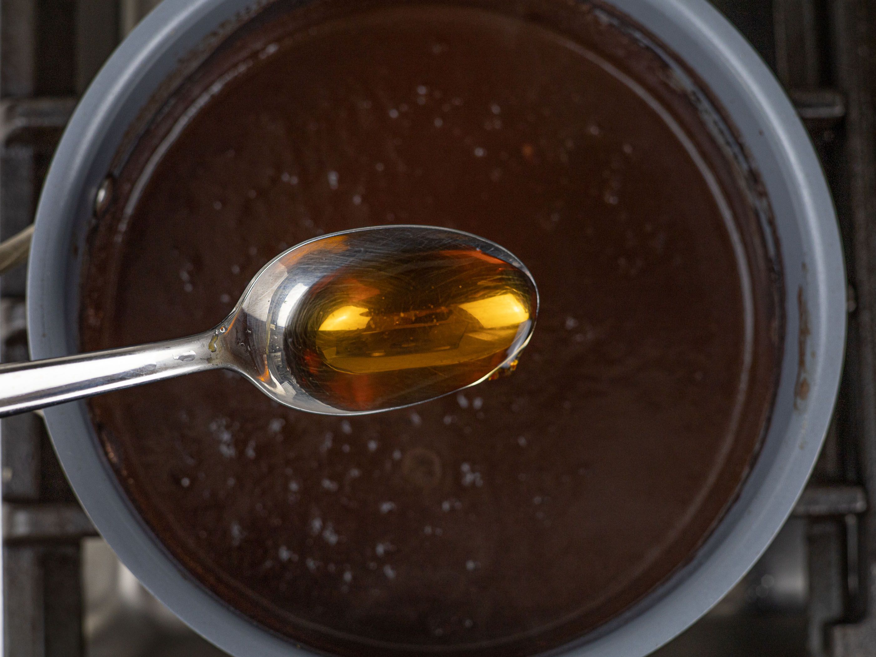 Spoon with fish sauce held over saucepan with pork blood sauce