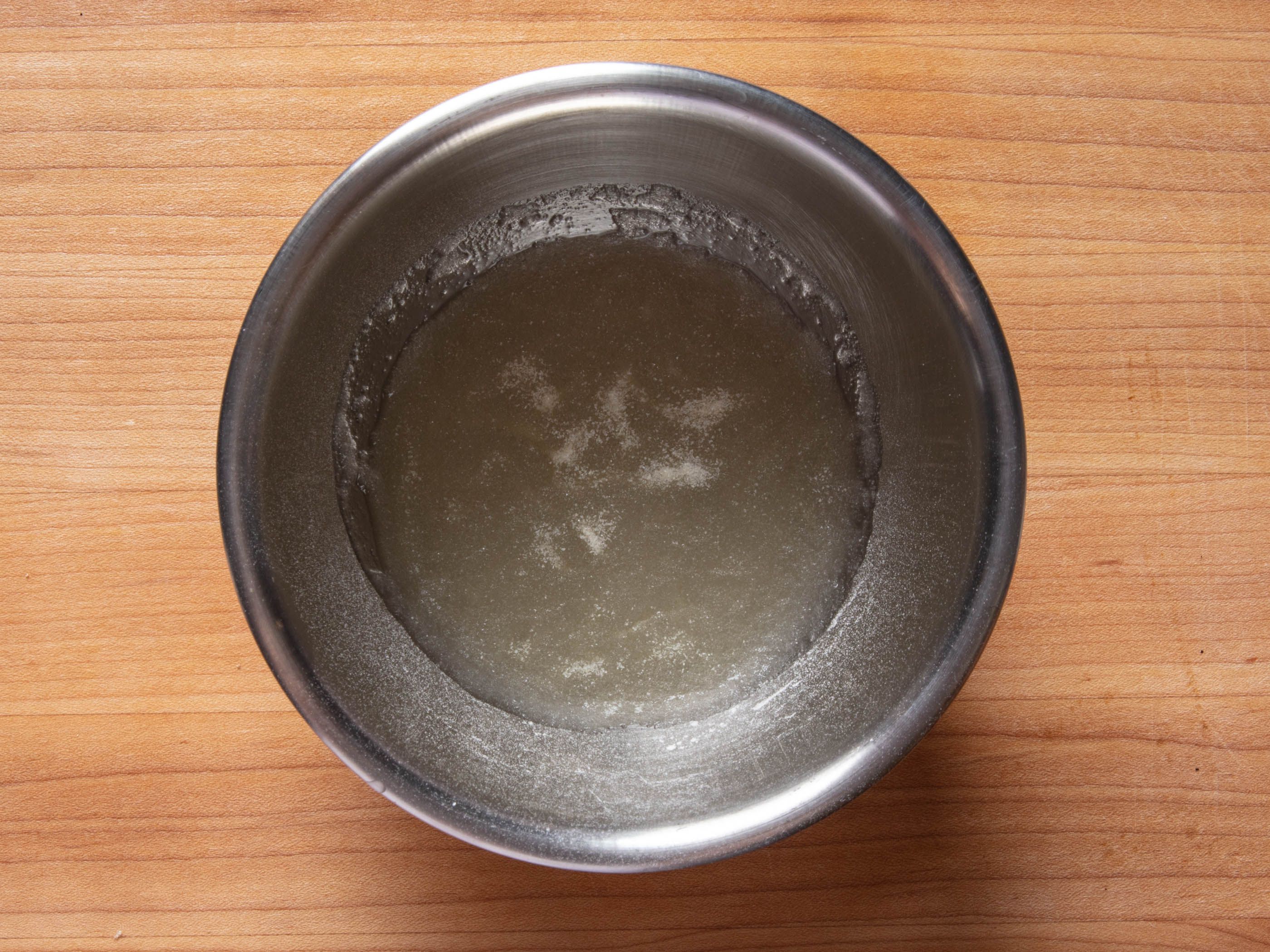 Gelatin bloomed in water in a small mixing bowl on a wooden counter