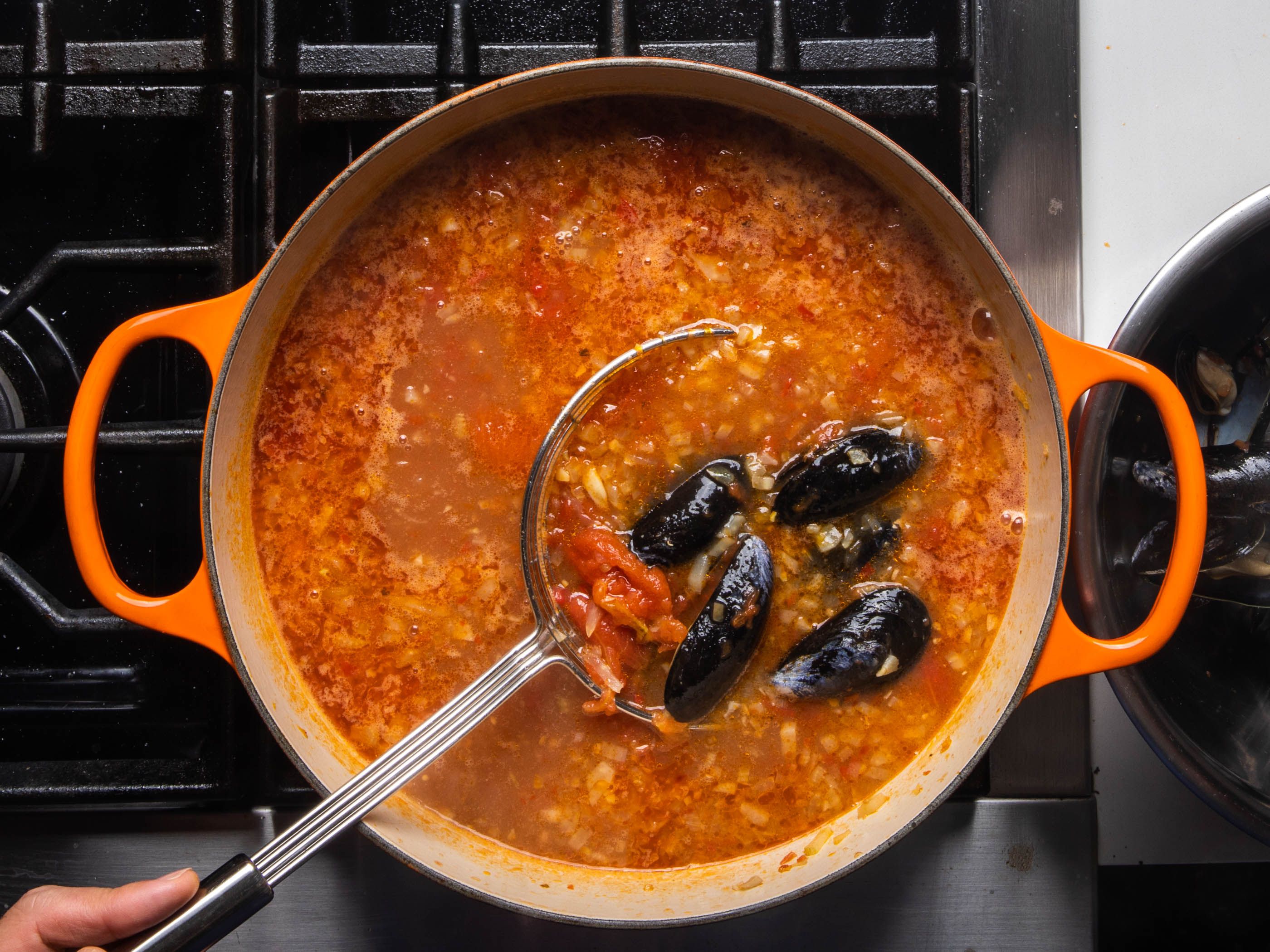 Removing the cooked mussels from the pot with a spider.