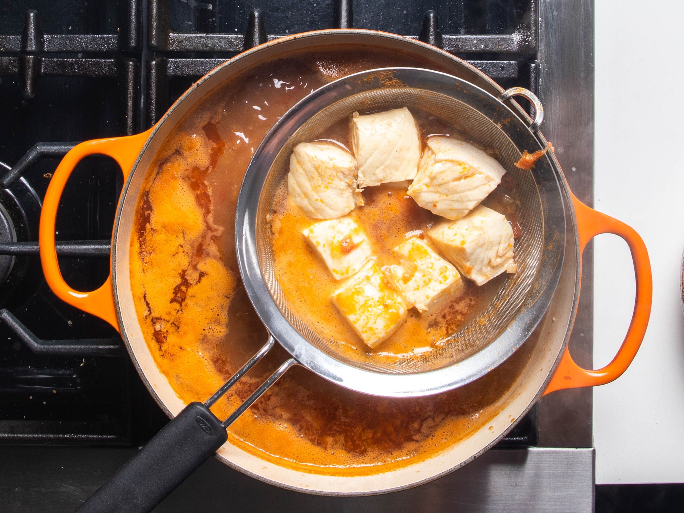 The cooked halibut in the strainer being lifter out of the broth.