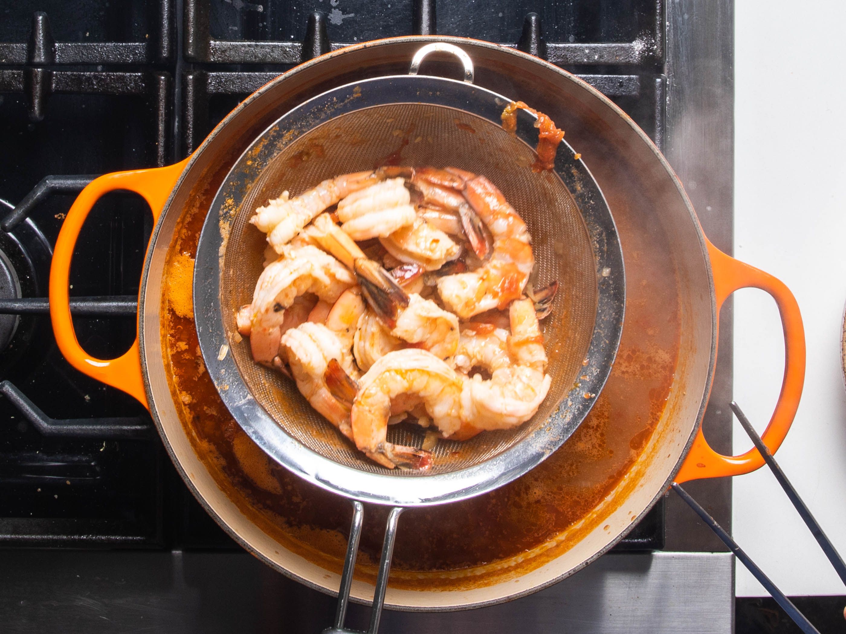 The cooked shrimp being lifted out of the broth while in the strainer basket.