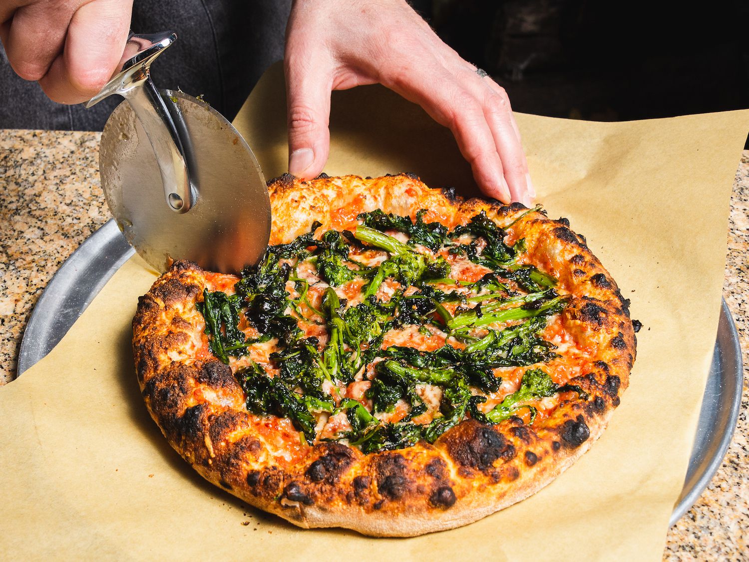Rotating a pizza with burst cherry tomatoes as it bakes in an outdoor pizza oven