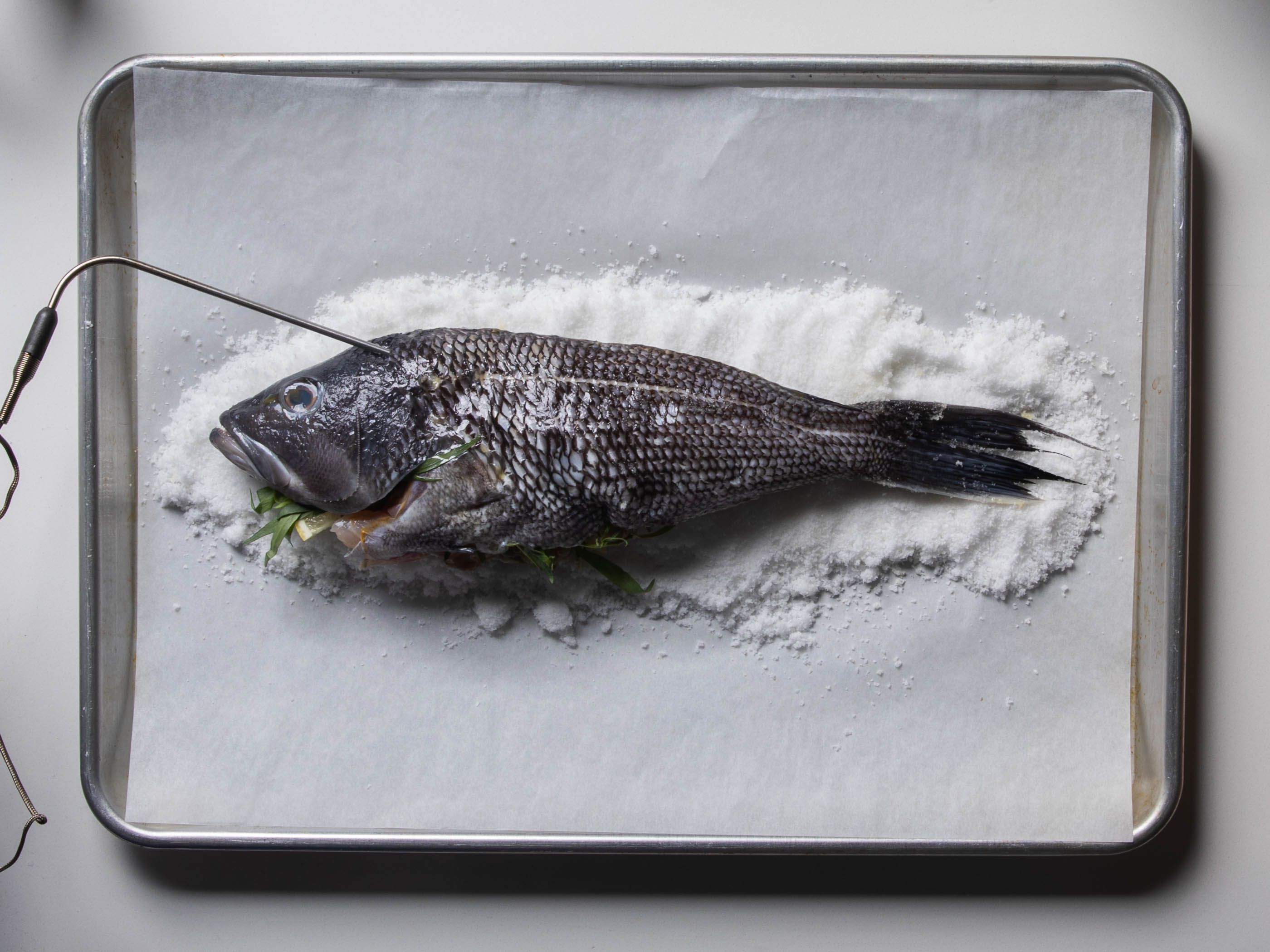 The whole fish is on the bed of salt, and a leave-in thermometer probe has been inserted into the thickest part of the fillet just behind the head.