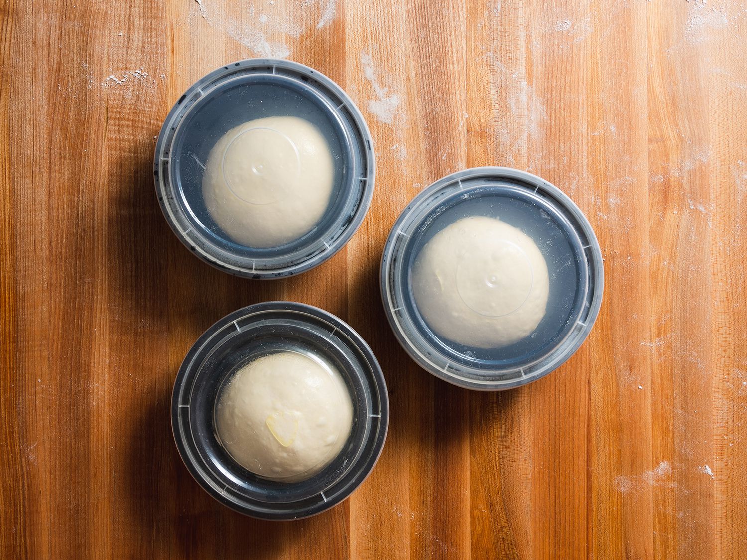 Pizza dough balls in three takeout containers on a wooden surface