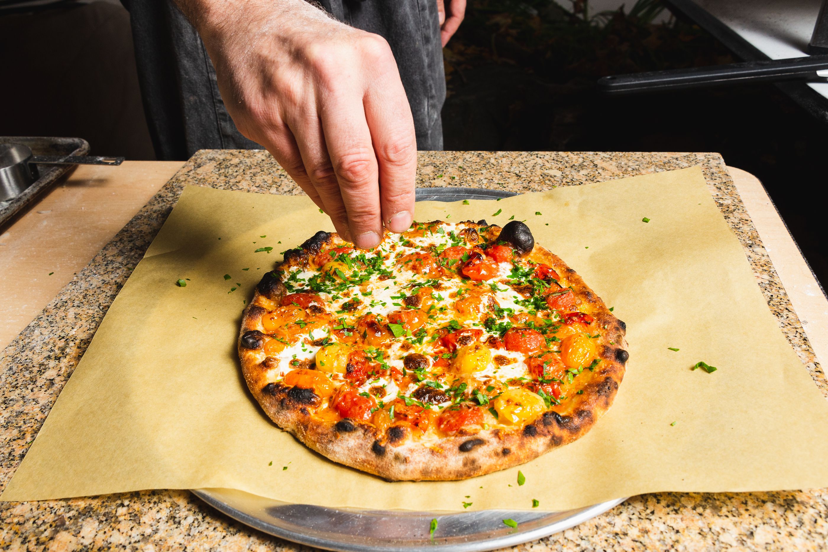 Burst cherry tomato outdoor pizza oven being sprinkled with herbs