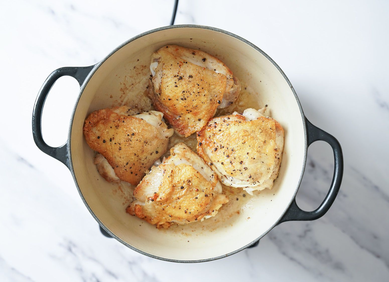 Seasoned, slightly browned chicken in a Dutch oven.
