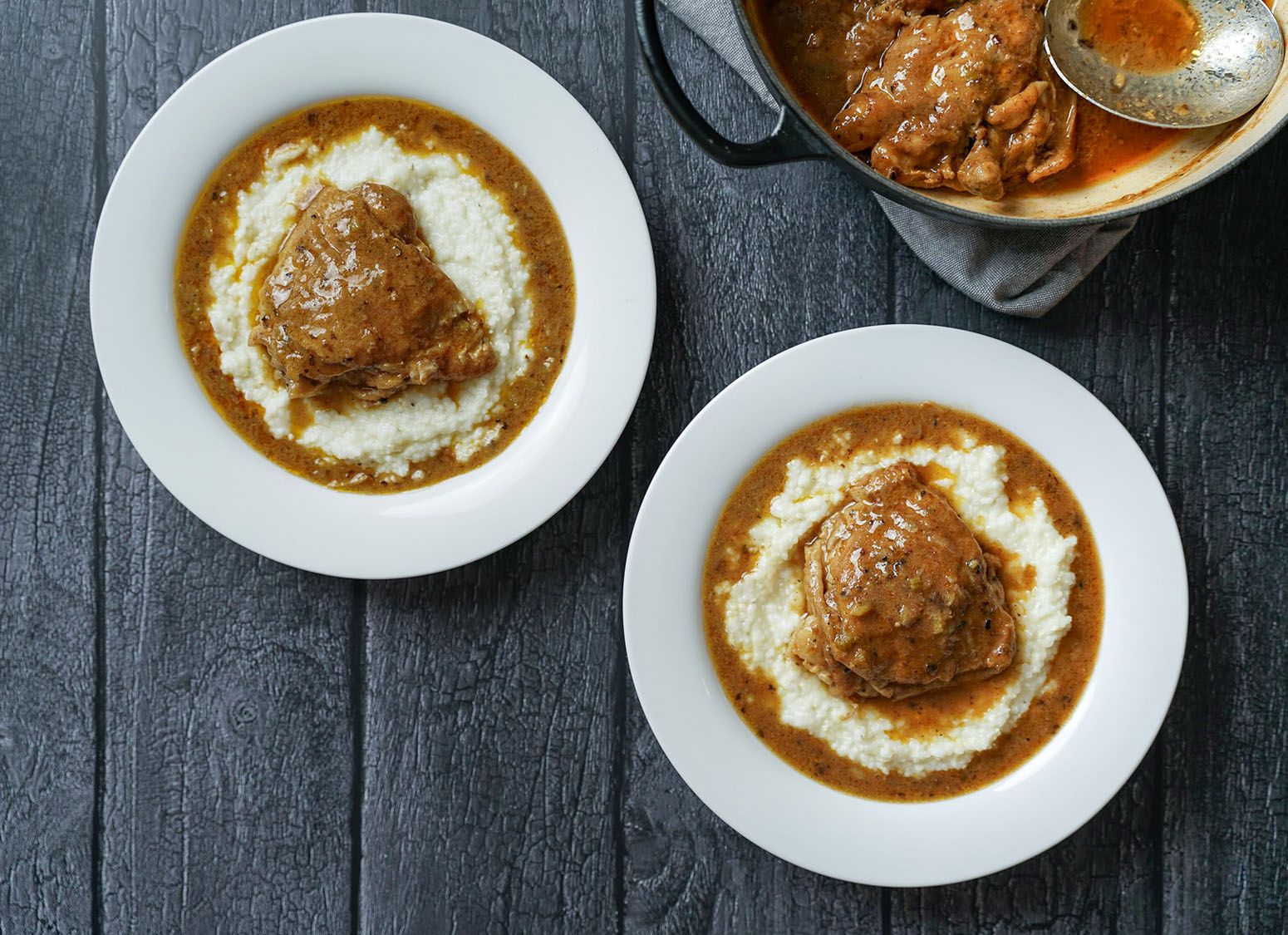 Chicken atop grits in white bowls.