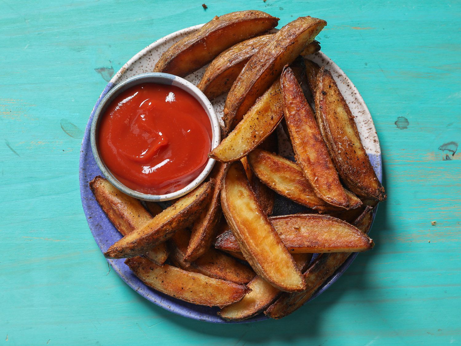 Overhead of a plate of potato wedges with a ramekin of ketchup.