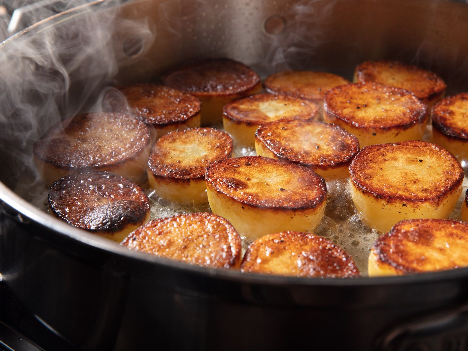 Potatoes in a pan that have been seared on one side, with butter foaming.