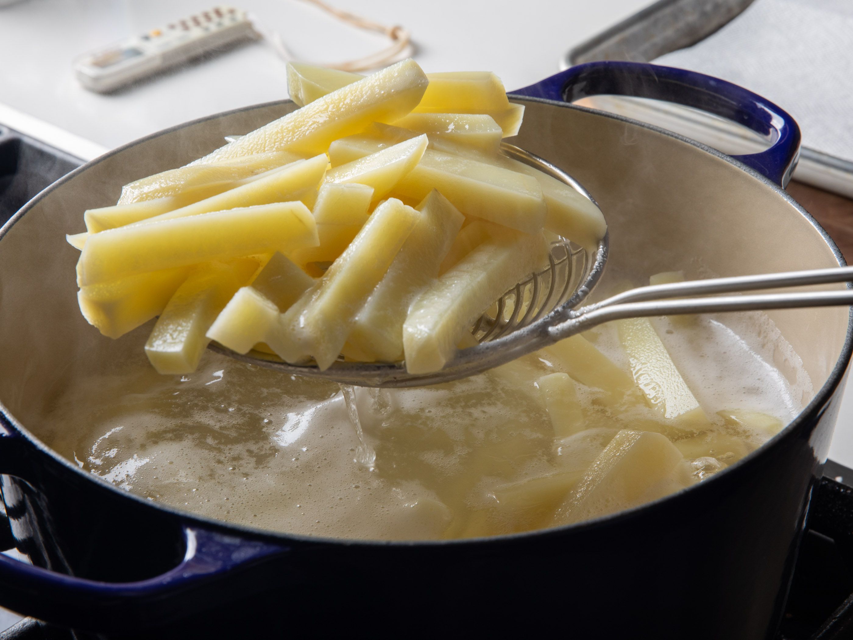 Fries being lifted out of a pot of simmering vinegar water.