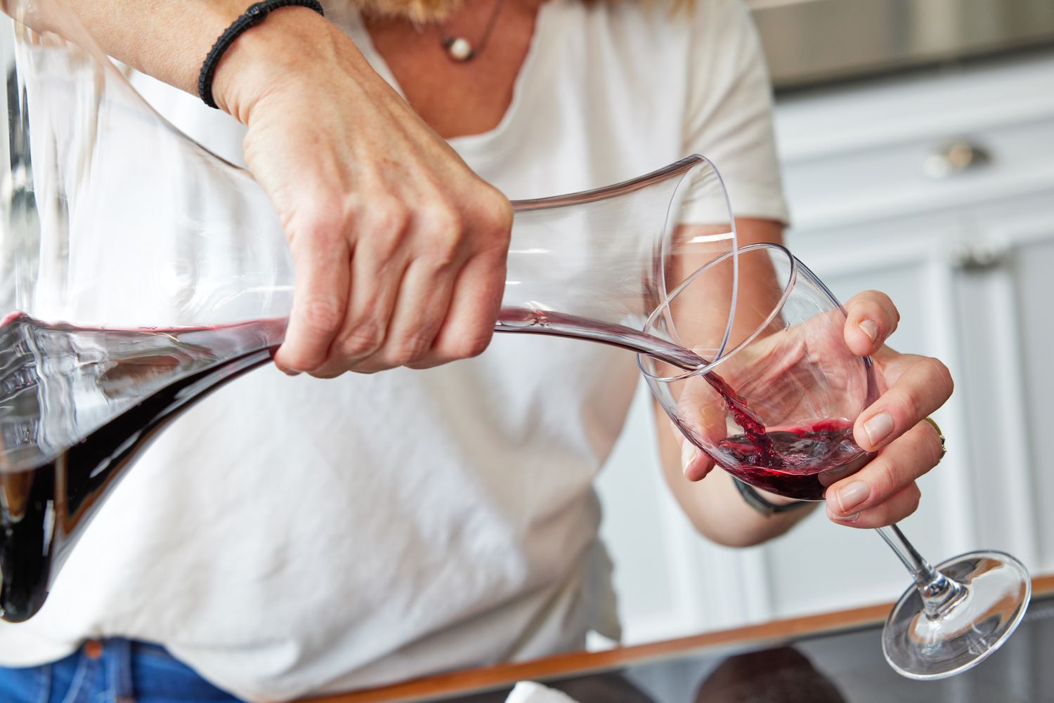 A closeup of a hand pouring red wine from a standard decanter into a wine glass
