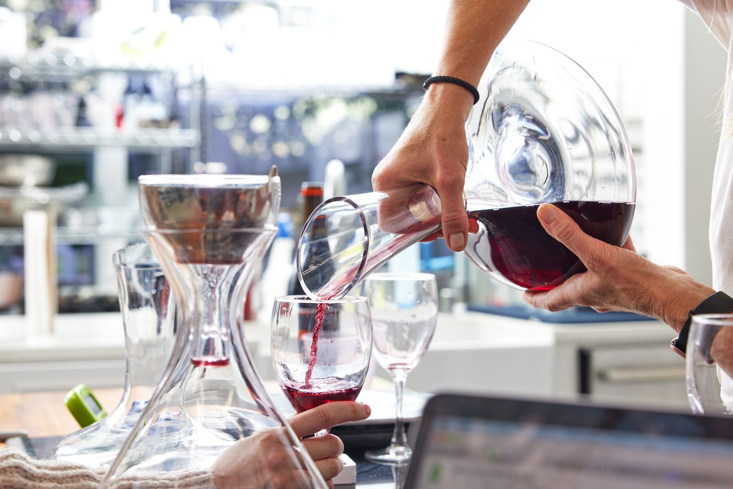 A hand pouring red wine from a standard decanter into a wine glass