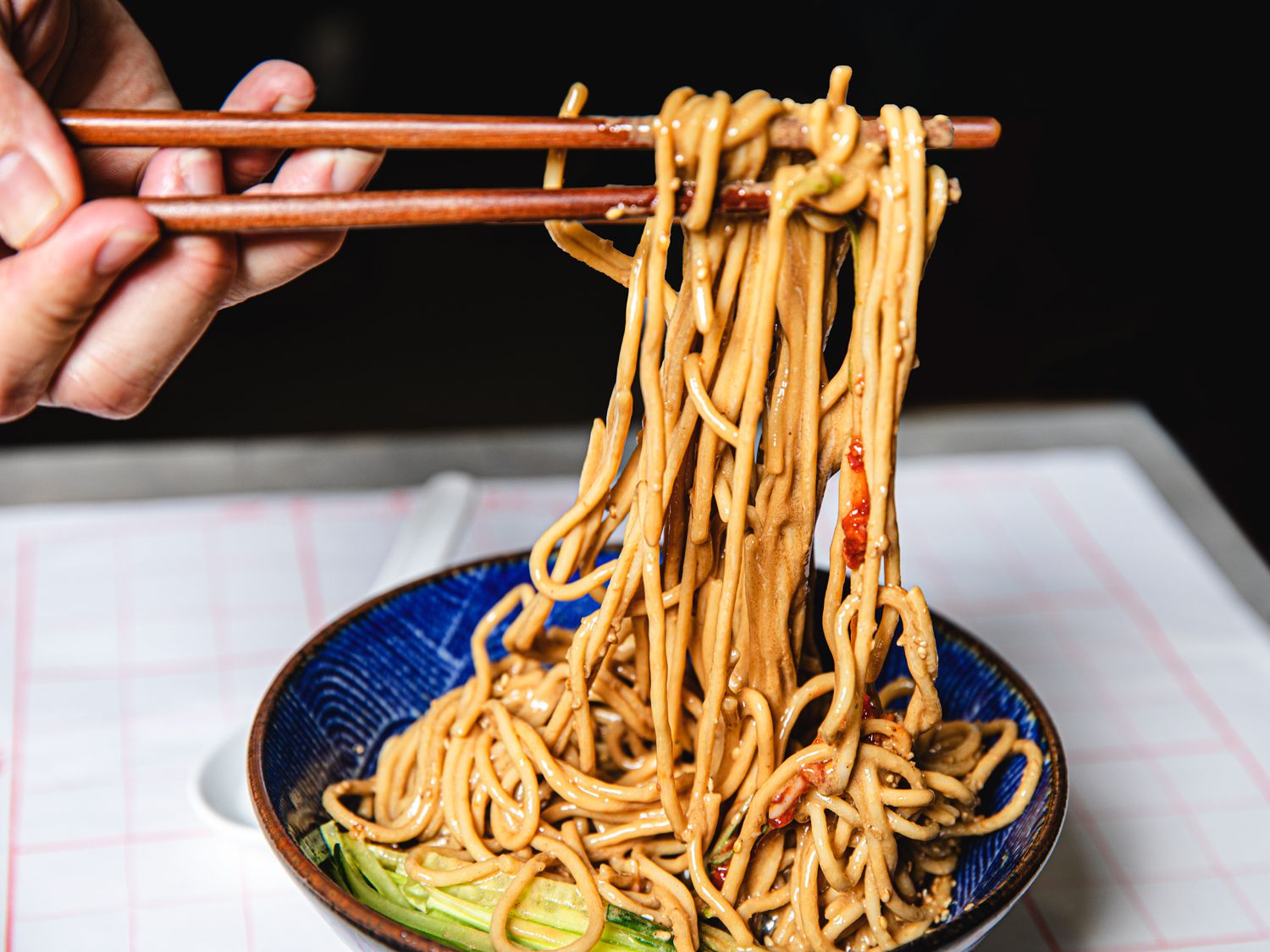 Sesame noodles being lifted out of blue bowl
