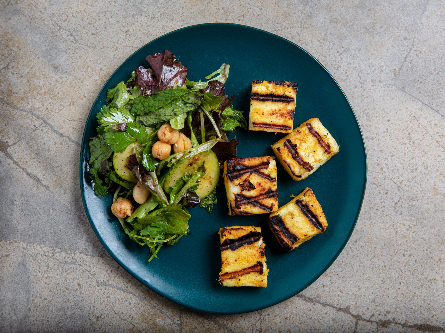Overhead view of grilled paneer and chickpea salad on a blue plate on a grey marbled backdrop