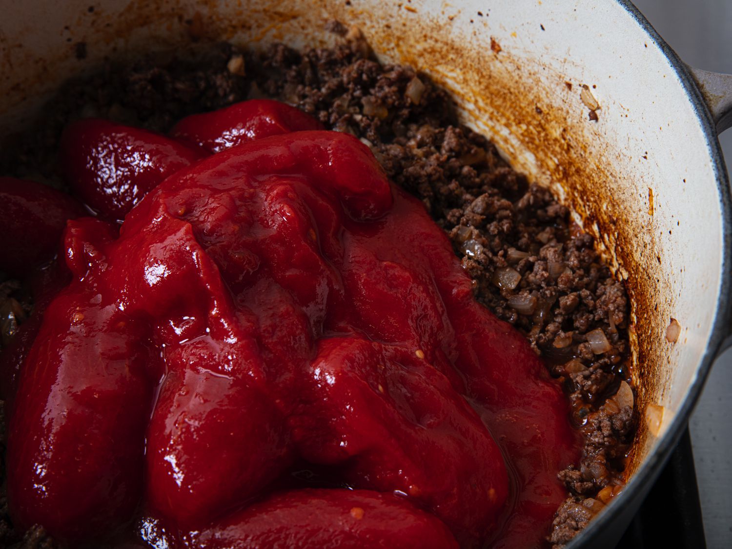 Overhead view of canned tomatoes added to meat in pot