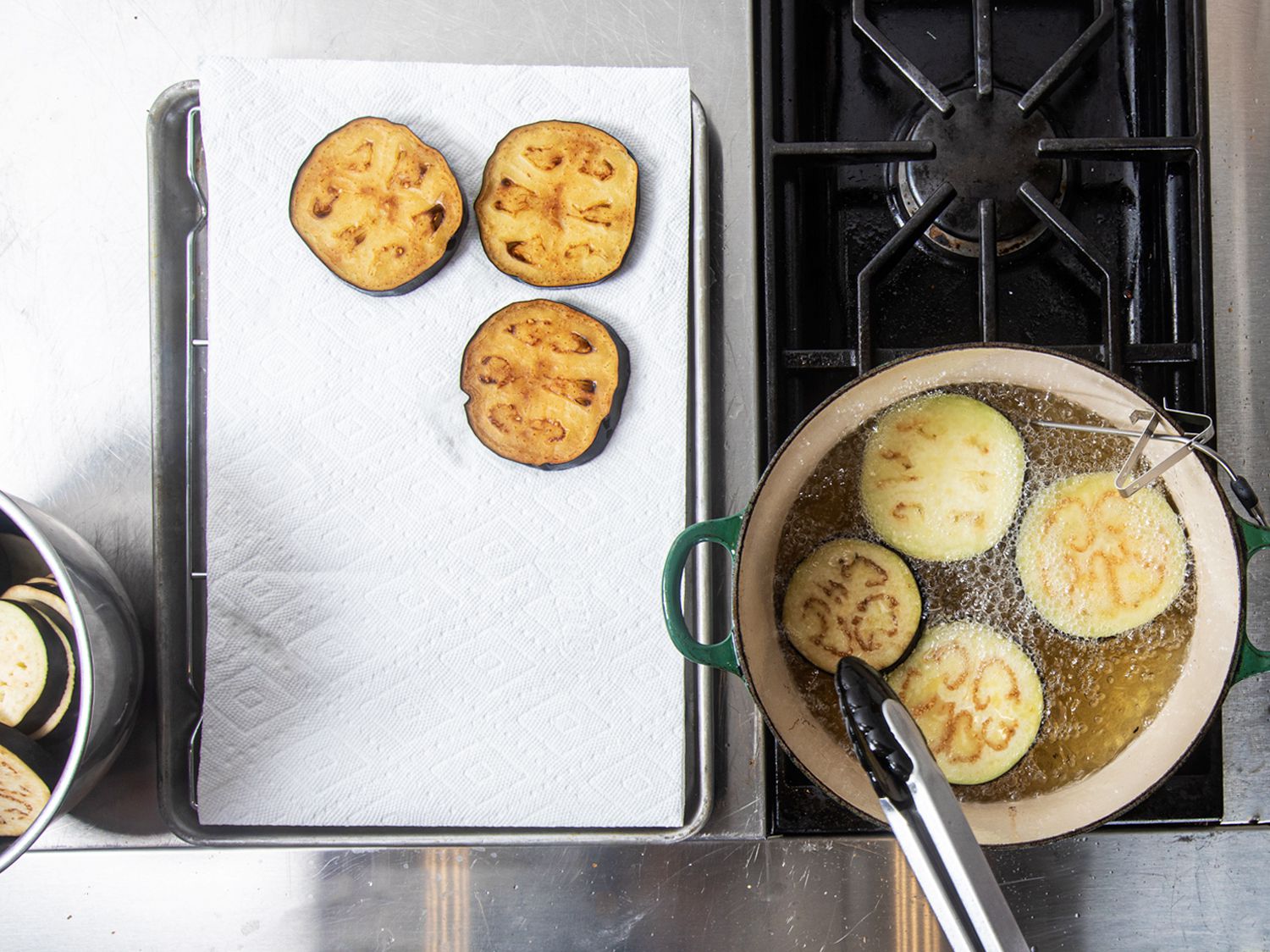 Overhead view of eggplants being fried in a dutch oven with 3 resting on a paper towel to the side