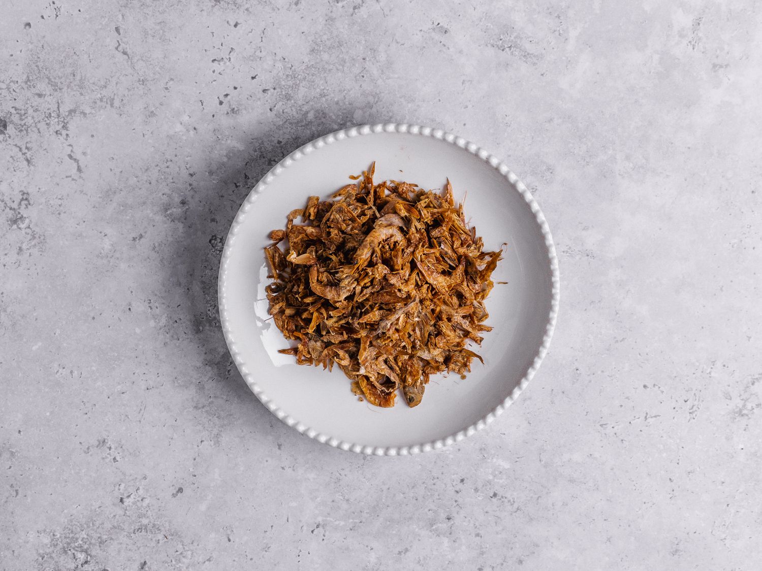 Dried crayfish in a white bowl on a marbled grey background