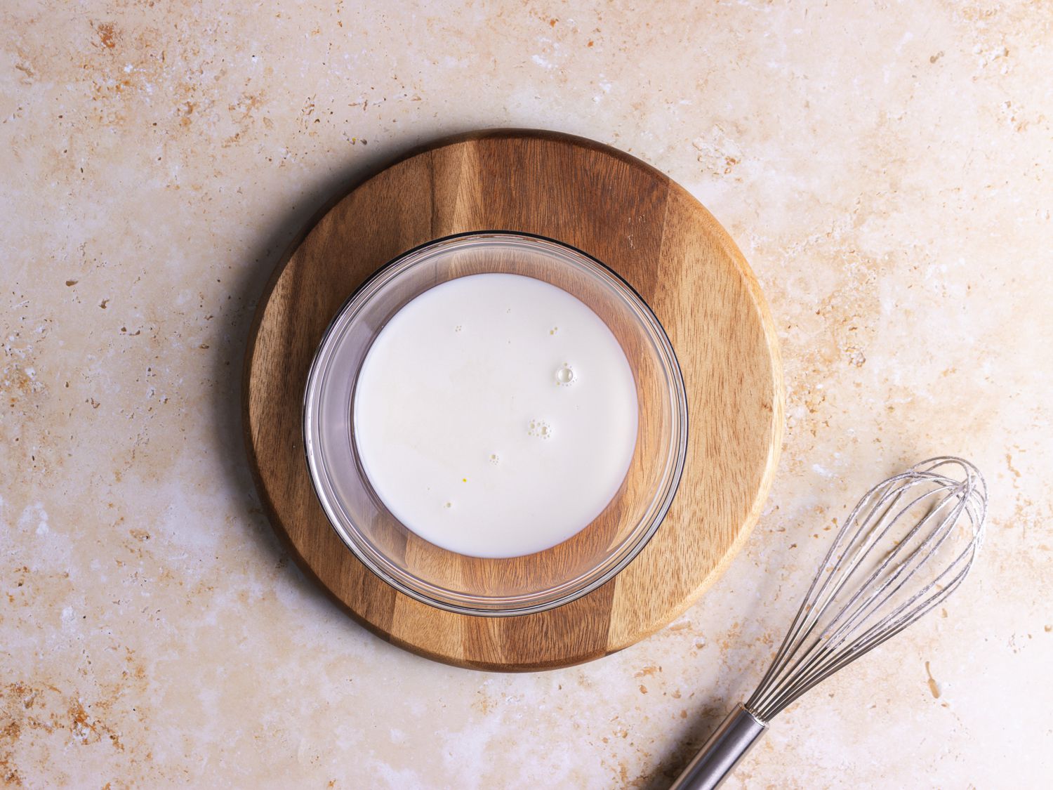Milk and vanilla in a bowl on a wooden plate with a whisk in frame