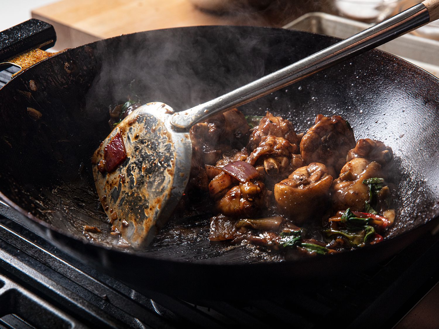 Close up image of a metal spatula moving braised chicken around a wok