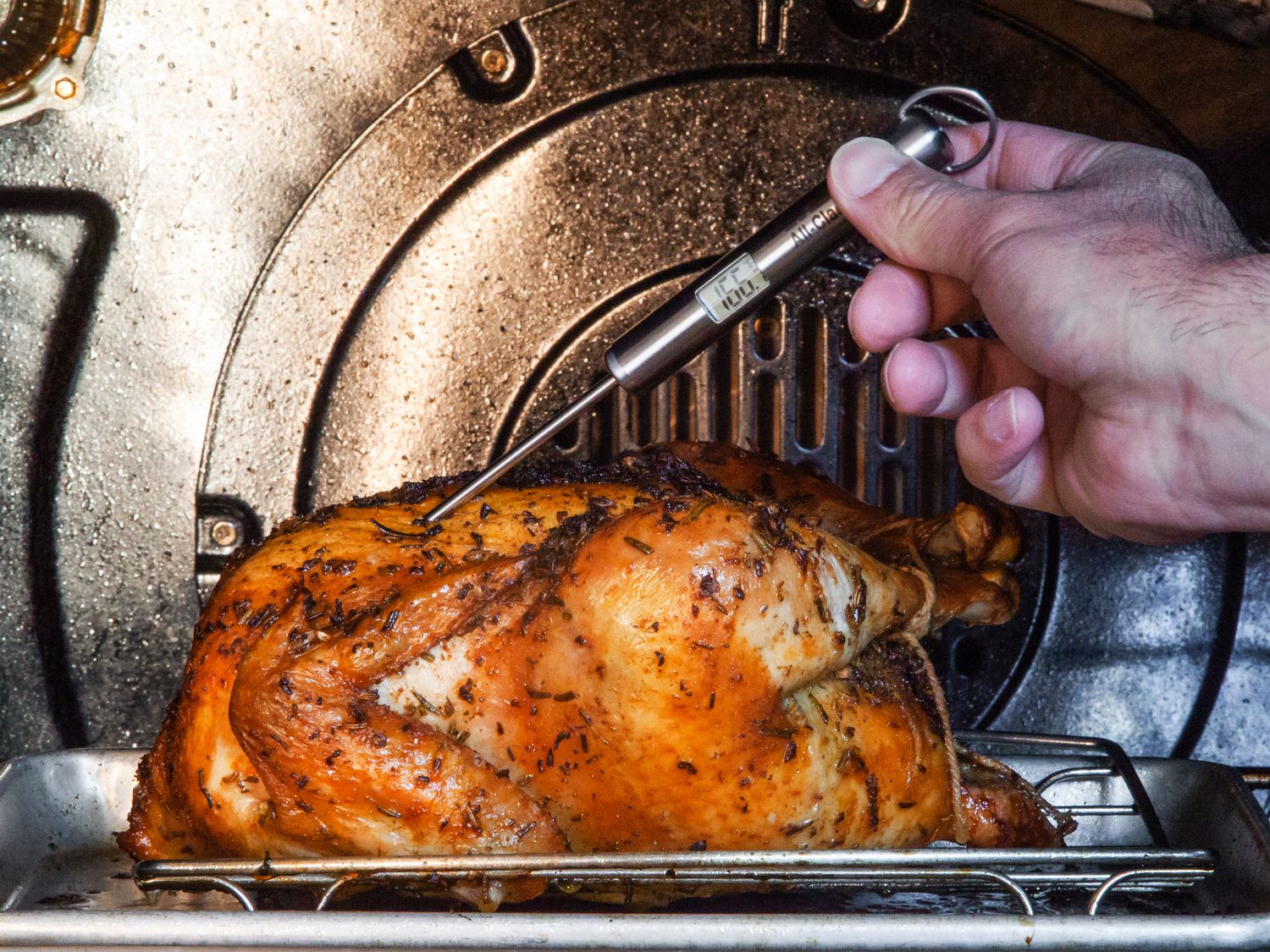 An All-Clad thermometer taking the temperature of a roast chicken in the oven