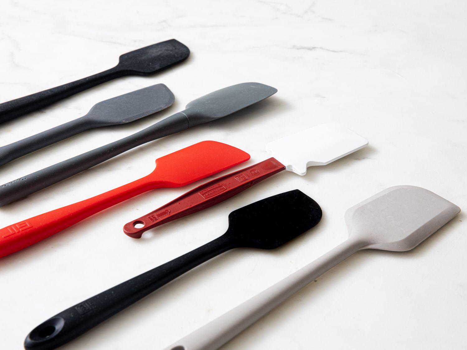 a side-angle view of seven silicone spatulas on a marble surface