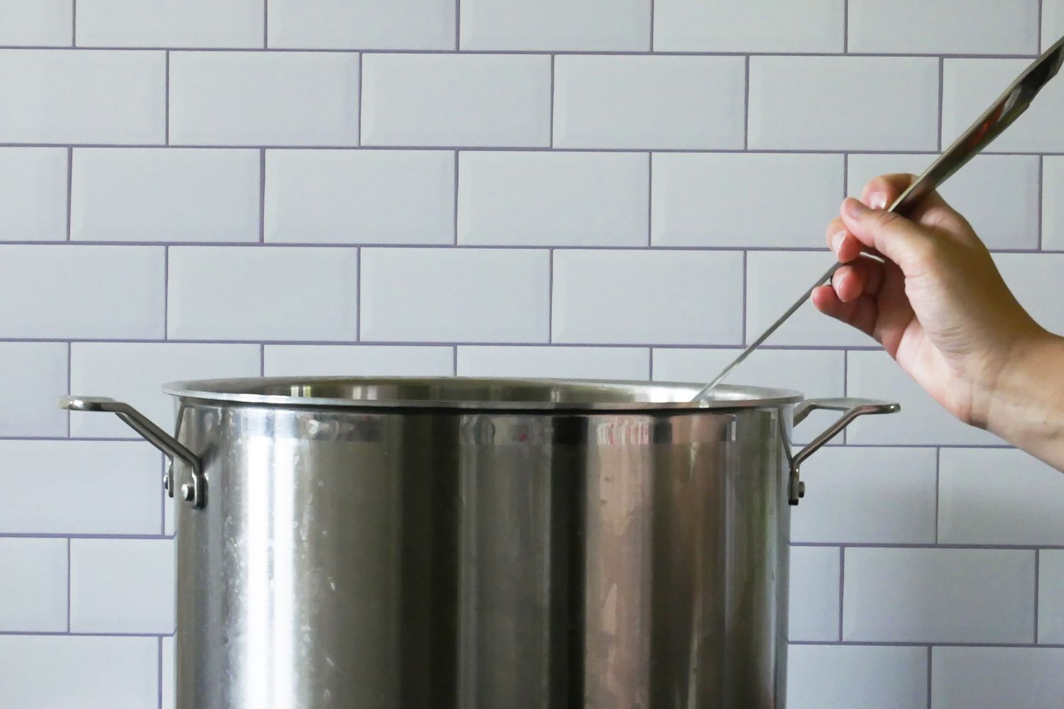 A hand holding the all clad ladle with the bowl in a large stock pot