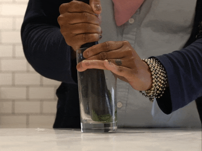 A GIF of a muddler muddling mint leaves in a tall cocktail glass