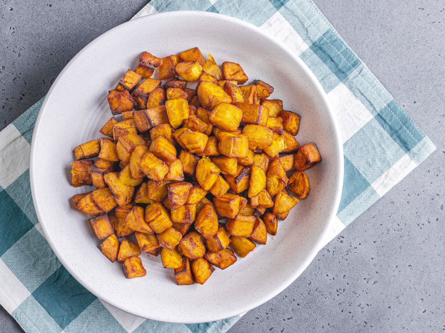 Cooked plantains in a white bowl on a blue checkered towel