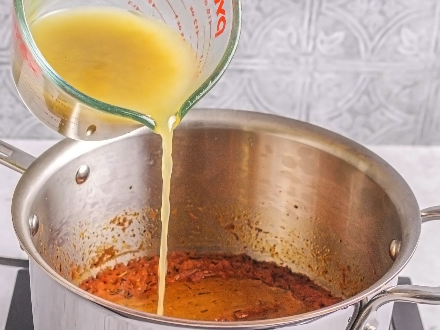 Stock being poured into pot of tomato puree