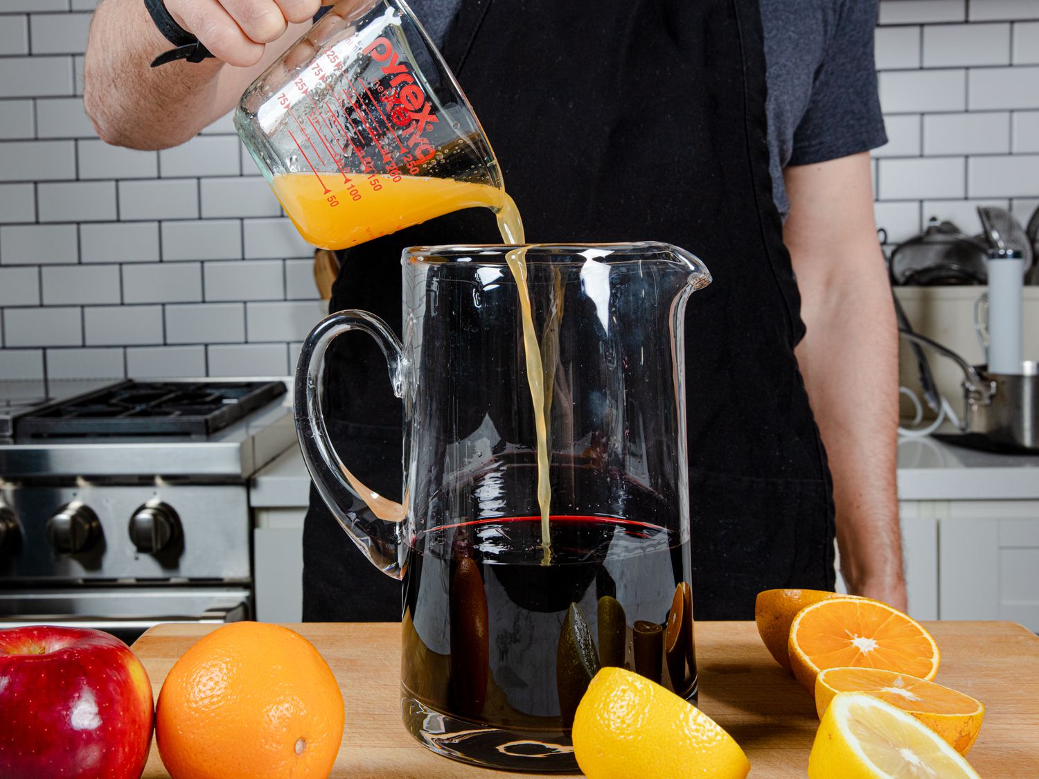 Red wine, liquor, and citrus juices combined in a large pitcher.