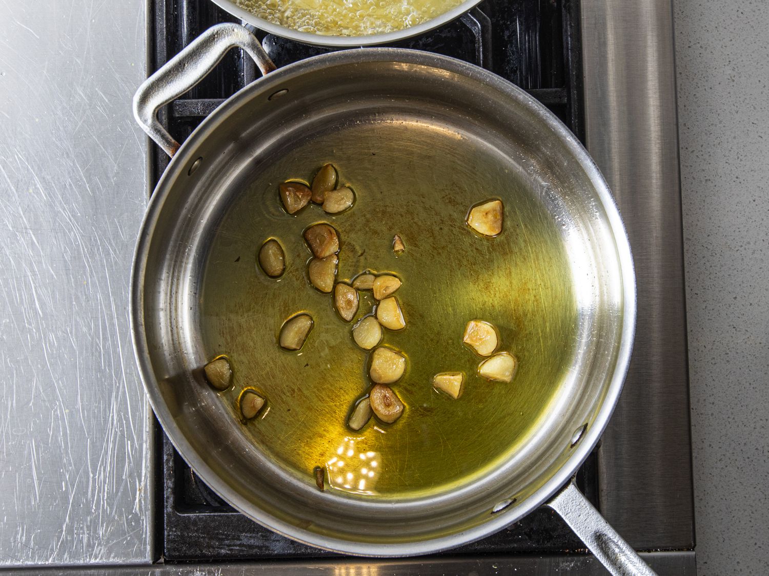 Whole or near-whole garlic cloves slowly cooking in olive oil in a pan