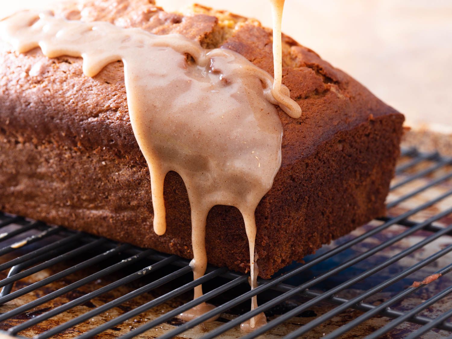 Pumpkin bread on a wire rack with glaze being poured onto it and dripping down the sides