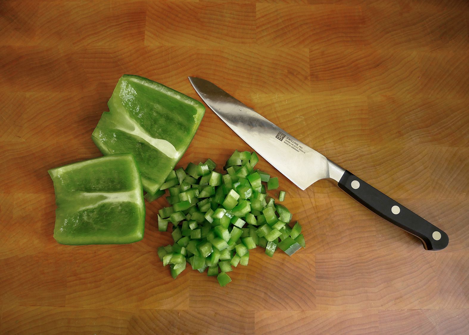 a knife on a cutting board with chopped up pieces of green bell pepper.