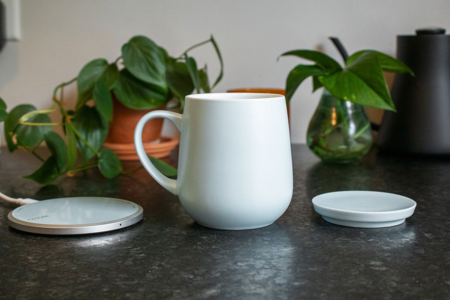 The OHOM mug with its lid off and its charging pad to the left