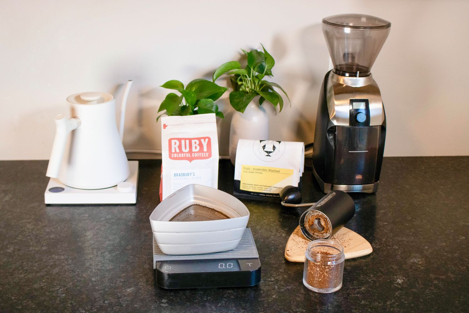 a handheld coffee grinder lays open next to a coffee sifter, kettle, and electric grinder