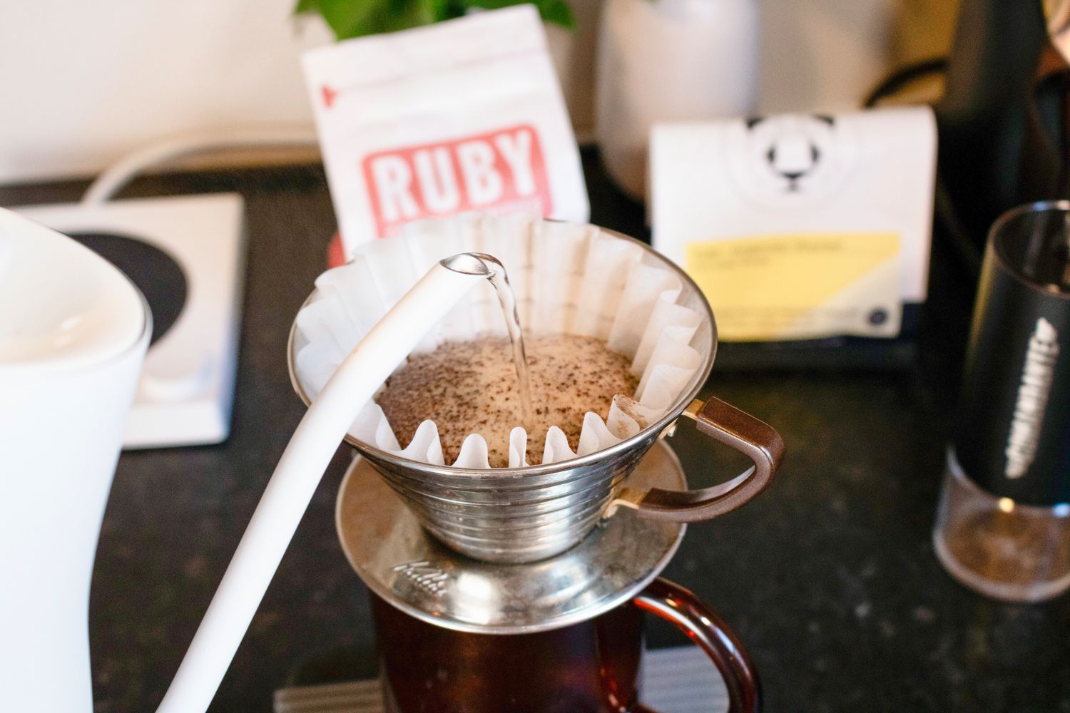 a gooseneck kettle spout pours water over coffee in a pourover dripper