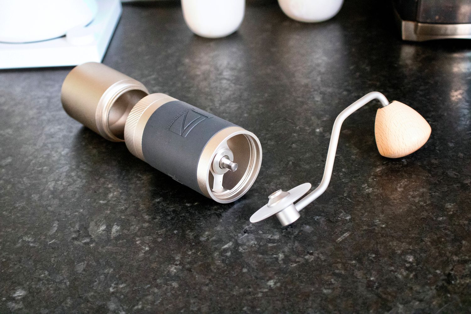 a hand held coffee grinder lies on a counter separated into its three parts