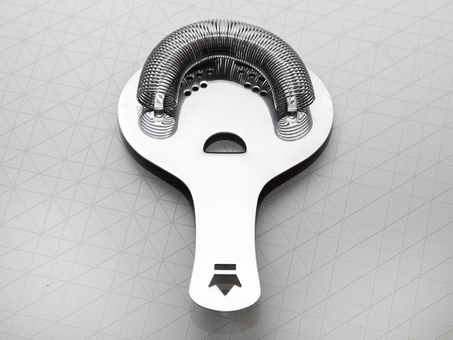 A stainless steel hawthorne strainer set on a grey surface