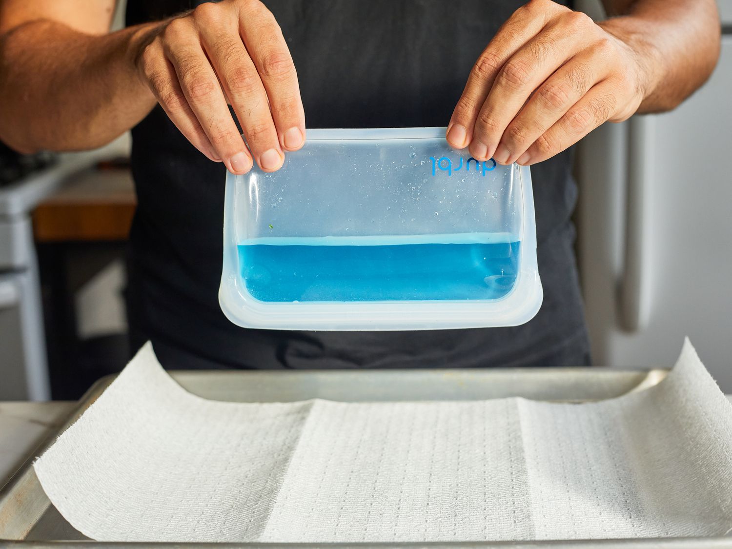 a person holding a reusable bag filled with water dyed blue to examine leakage.