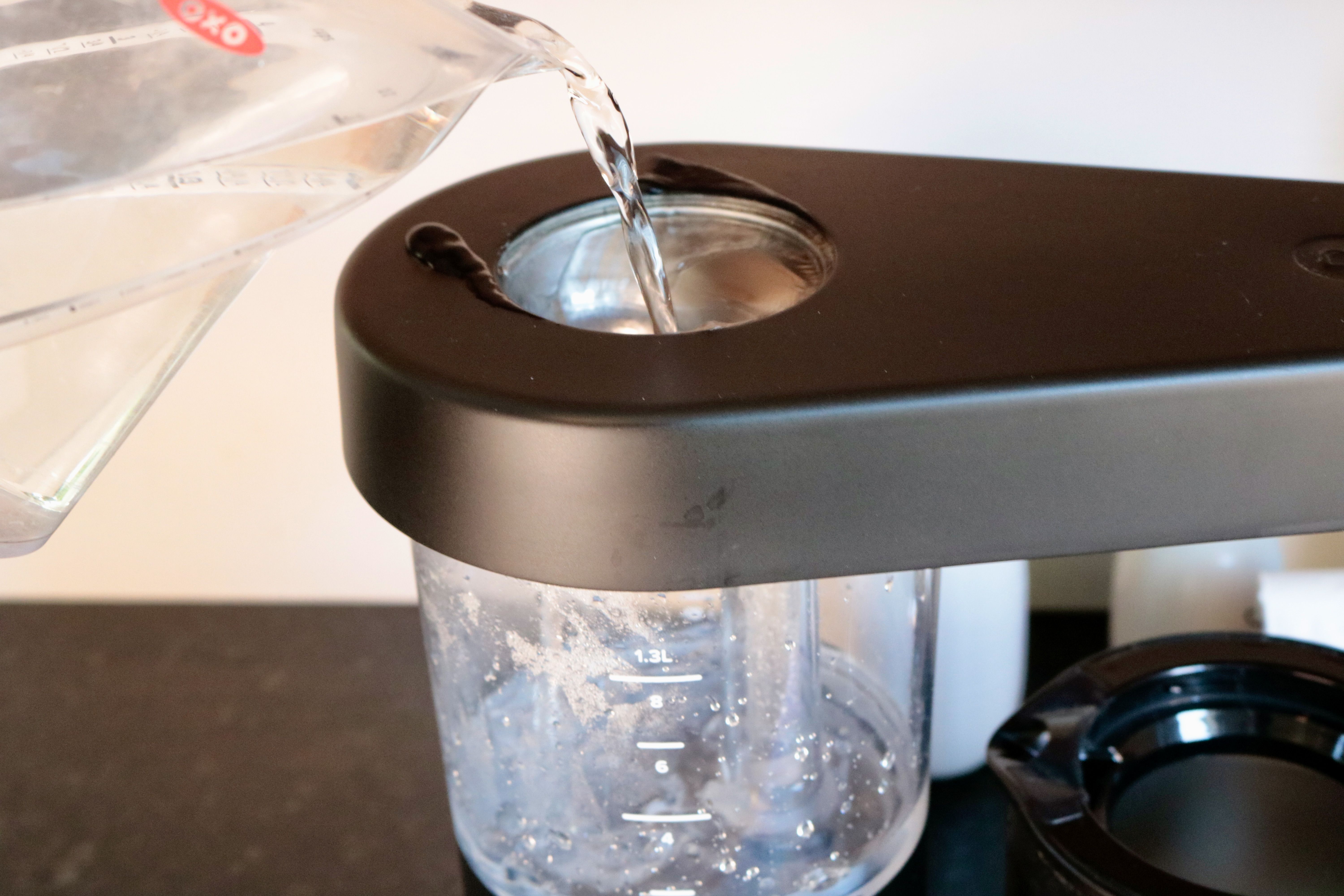 A measuring cup pouring water into a coffee maker's water reservoir