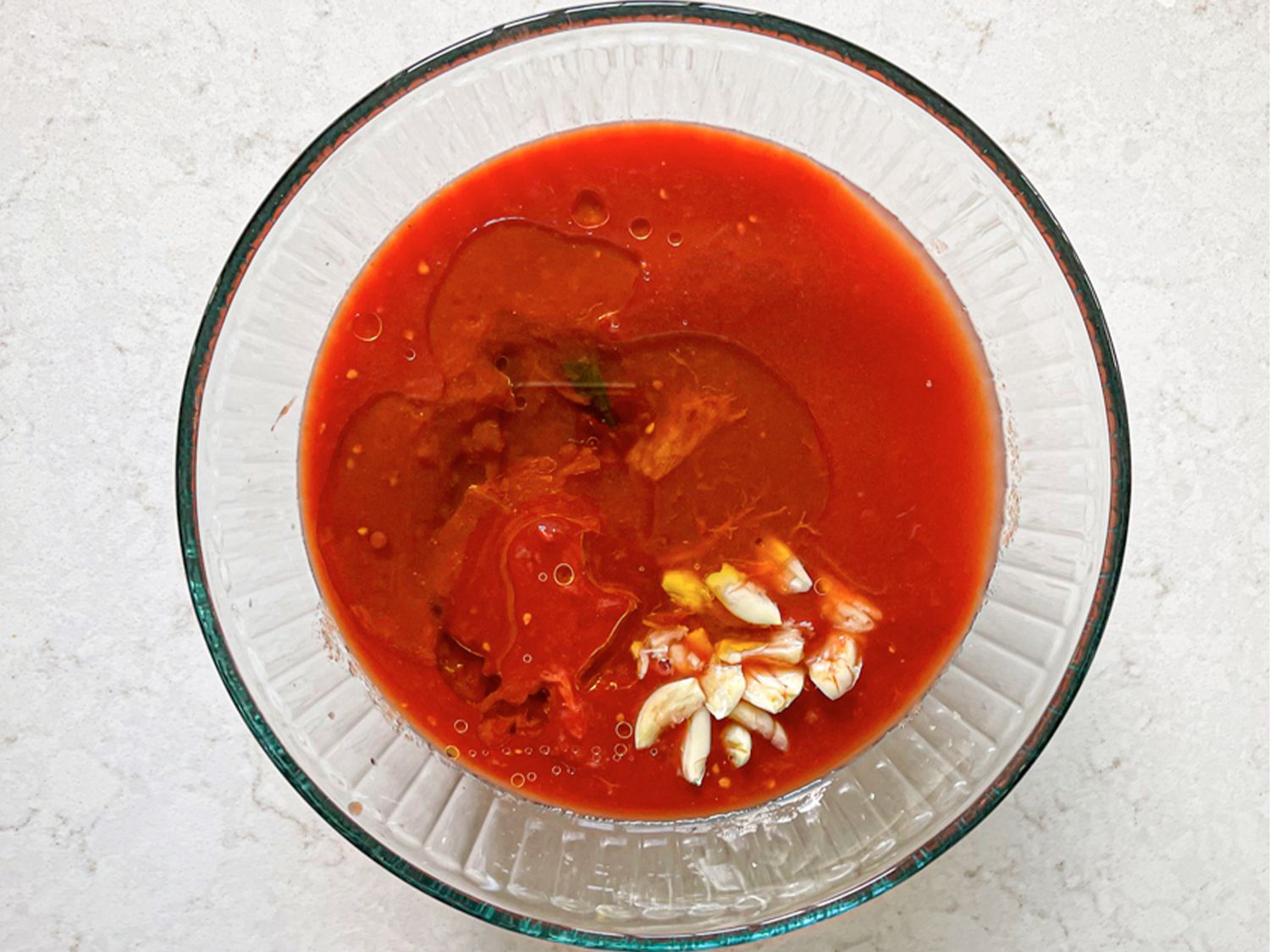 Crushed tomatoes topped with olive oil and garlic in a glass bowl