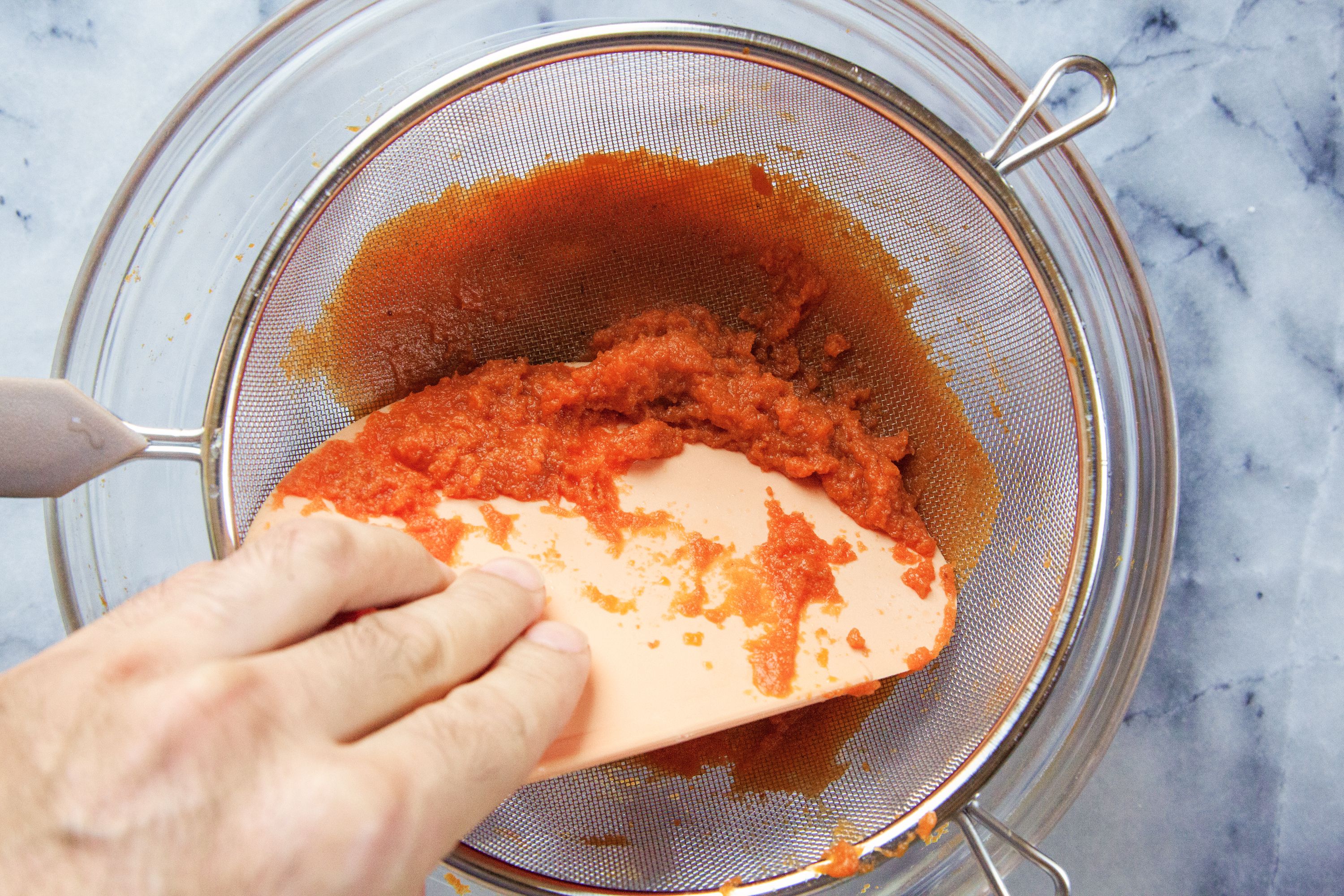 using the indigo bowl scraper to push pumpkin puree through a sieve.
