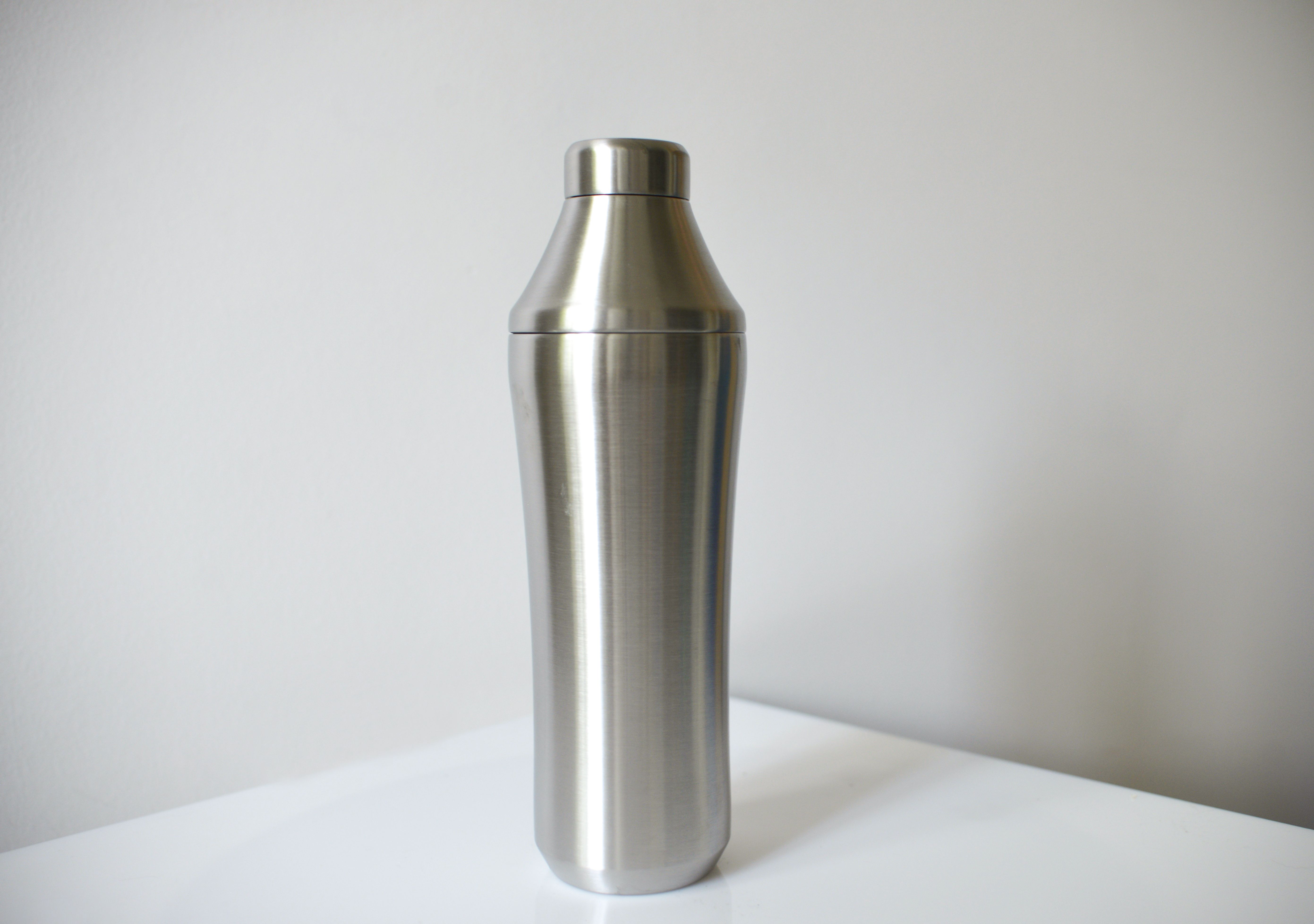 a tall stainless steel cocktail shaker against a white background and on a white countertop