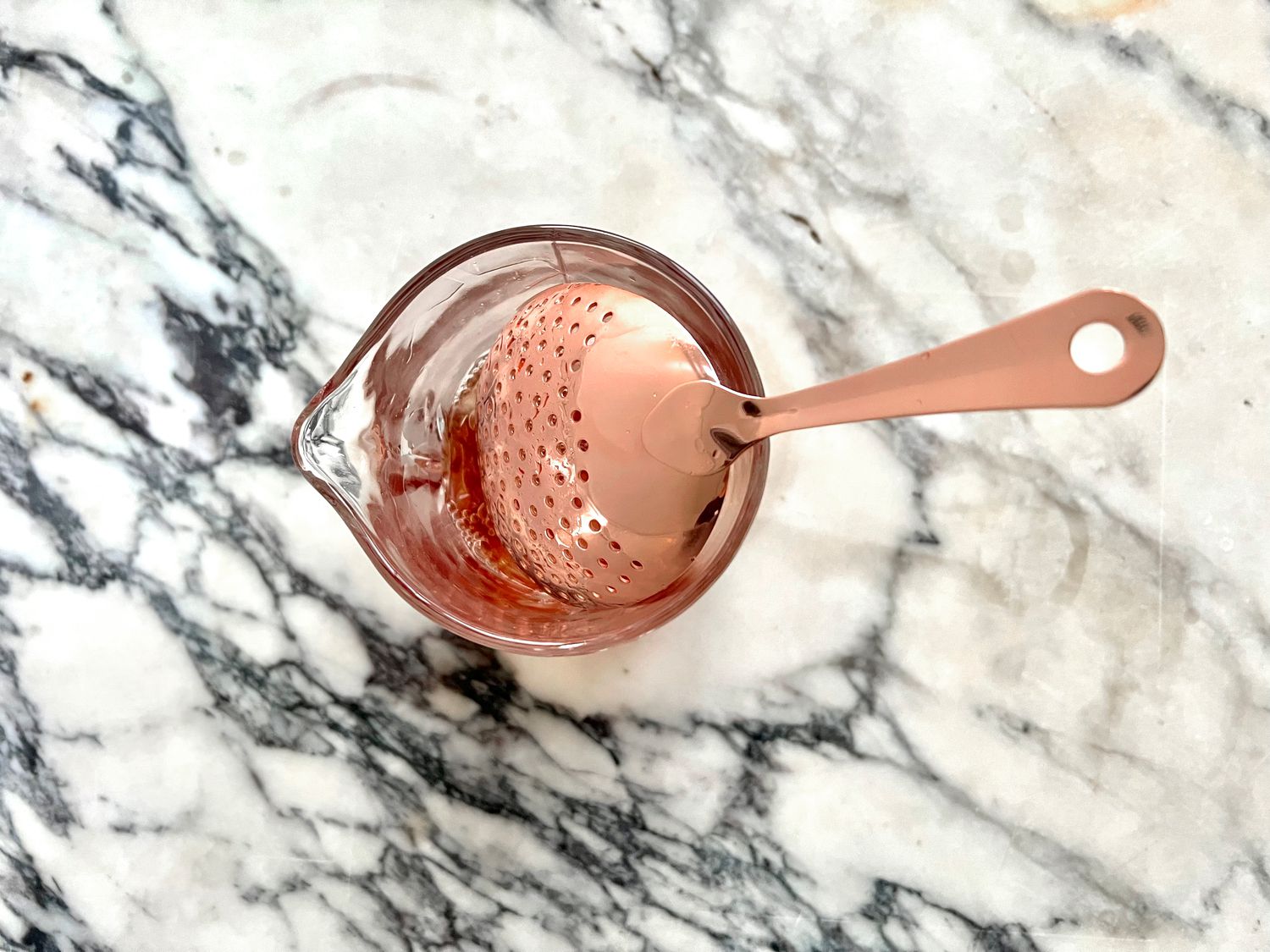the viski copper plated strainer in a mixing glass on a marble countertop.